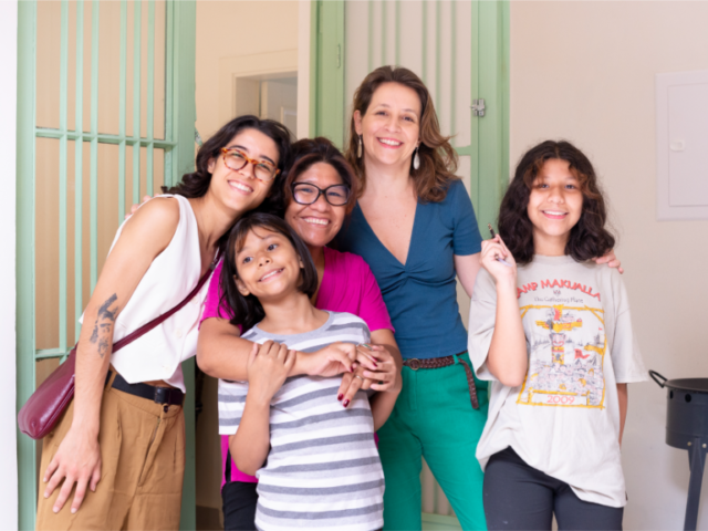 fica1 Group of five people of mixed ages and ethnicities smiling together in a doorway.