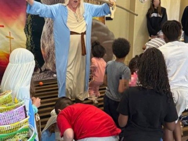 kidsmotelministry2 Person in a light blue robe and head covering performing a straw-snake gesture for a group of children indoors, with a painted backdrop behind them.